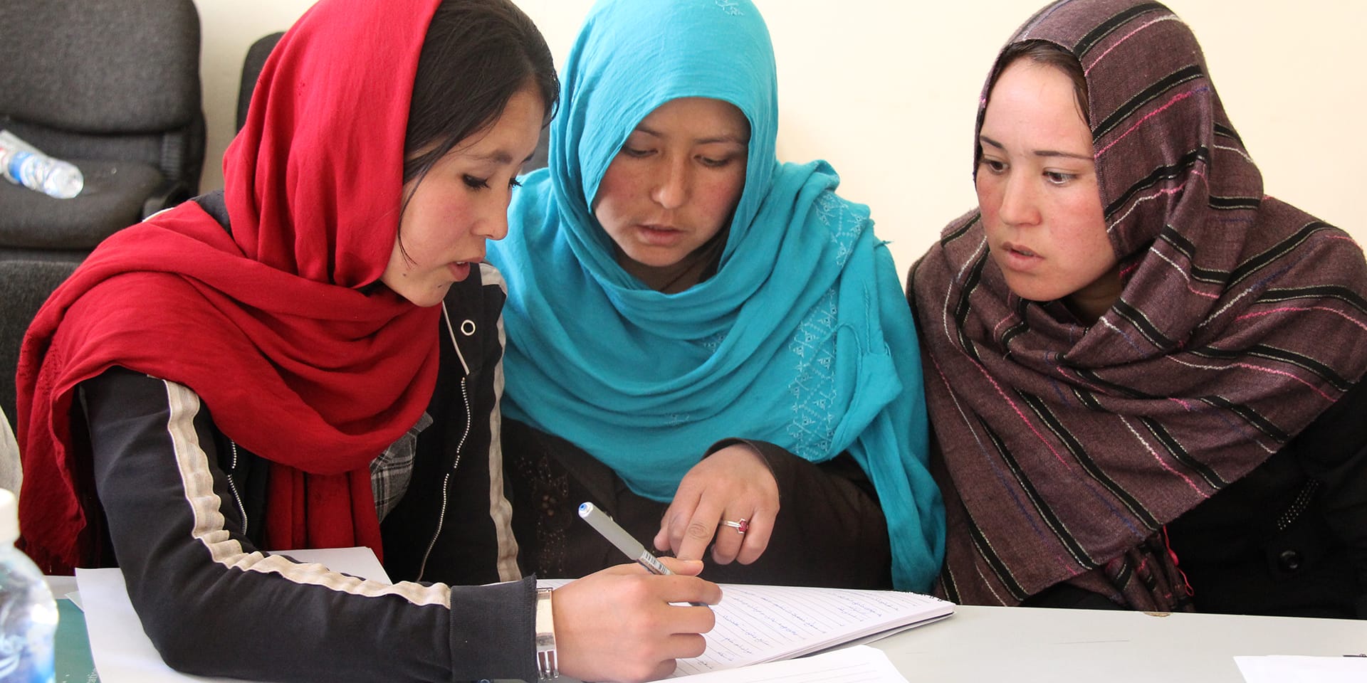 Image of two women reviewing a document while a third woman writes on it with a pen.