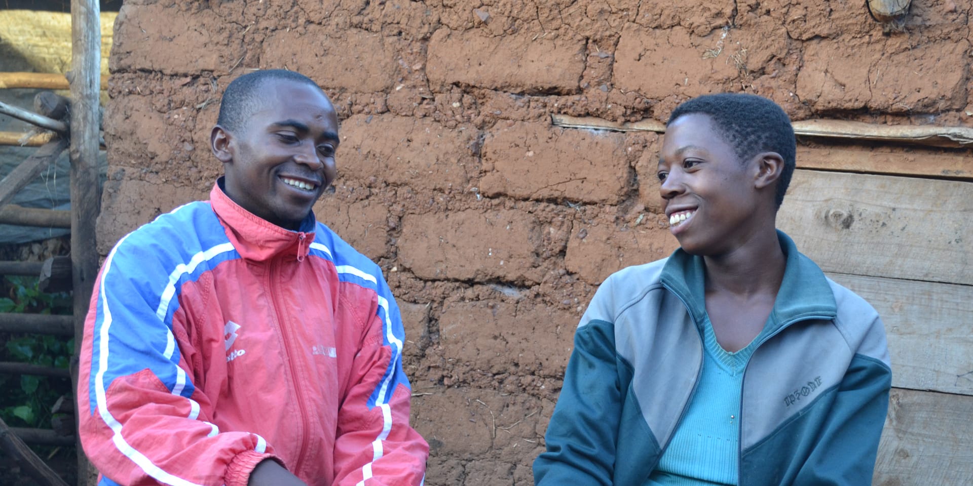 Image of two people sitting in front of a brick wall smiling as they talk.