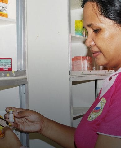 A woman holding and looking at a box of medication in a pharmacy.