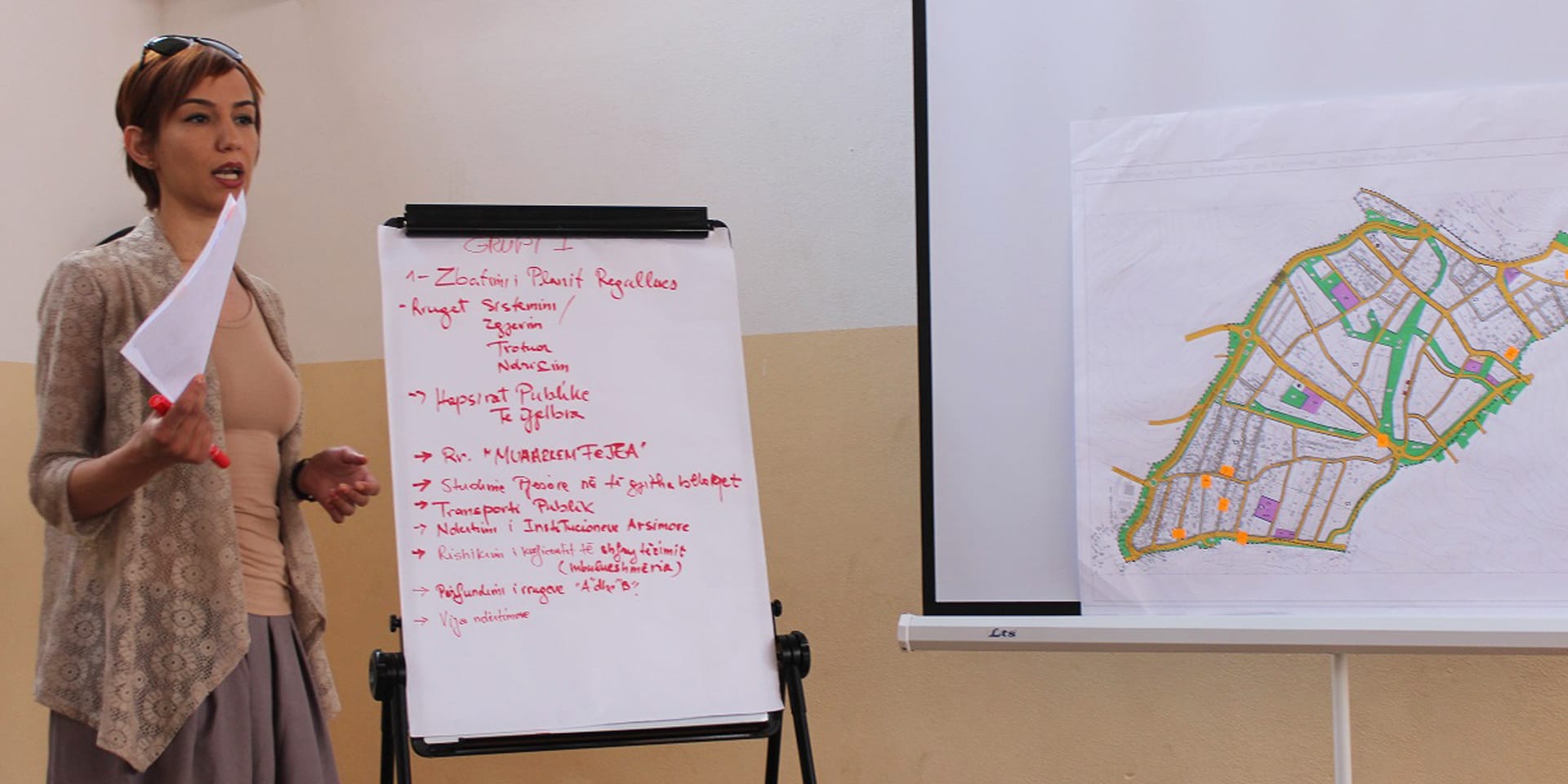 A woman giving a presentation that includes a whiteboard and a blueprint of a city.