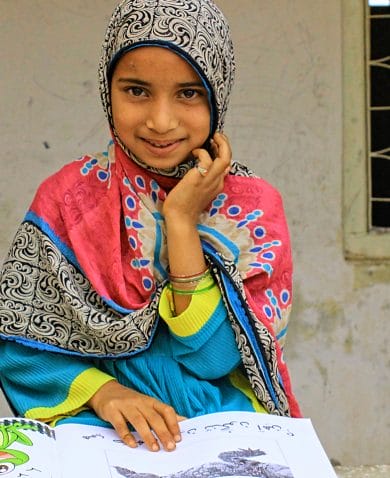 A smiling girl sitting in front of a home and reading from a children's book.