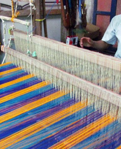 A man working on a loom producing vibrant blue and yellow cloth.