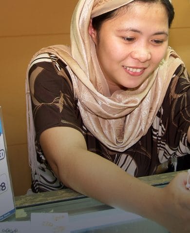 A smiling woman leaning forward on a glass display case while looking at her phone.
