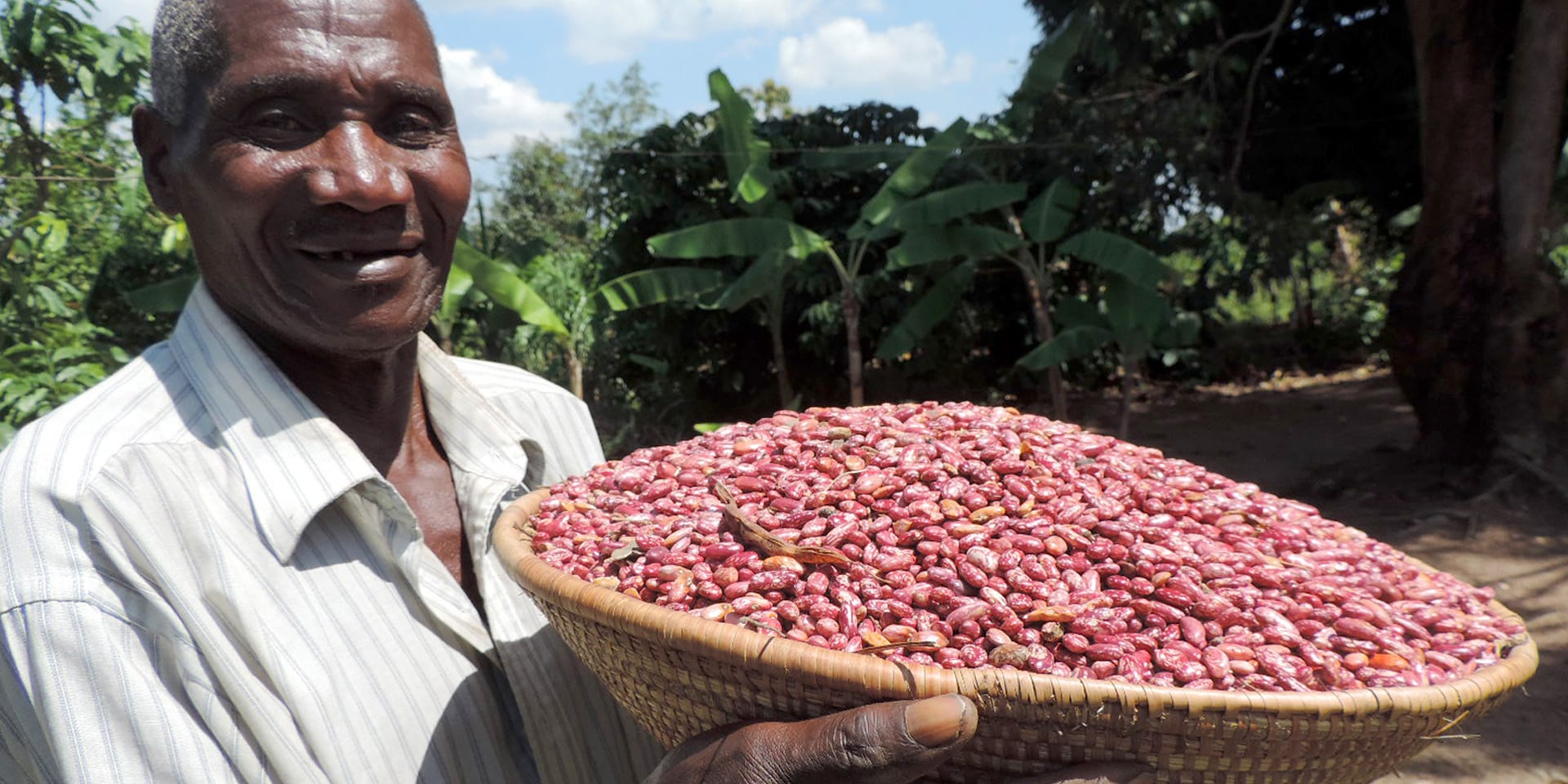 Image of a man smiling and holding a large woven basket filled with red-colored beans.
