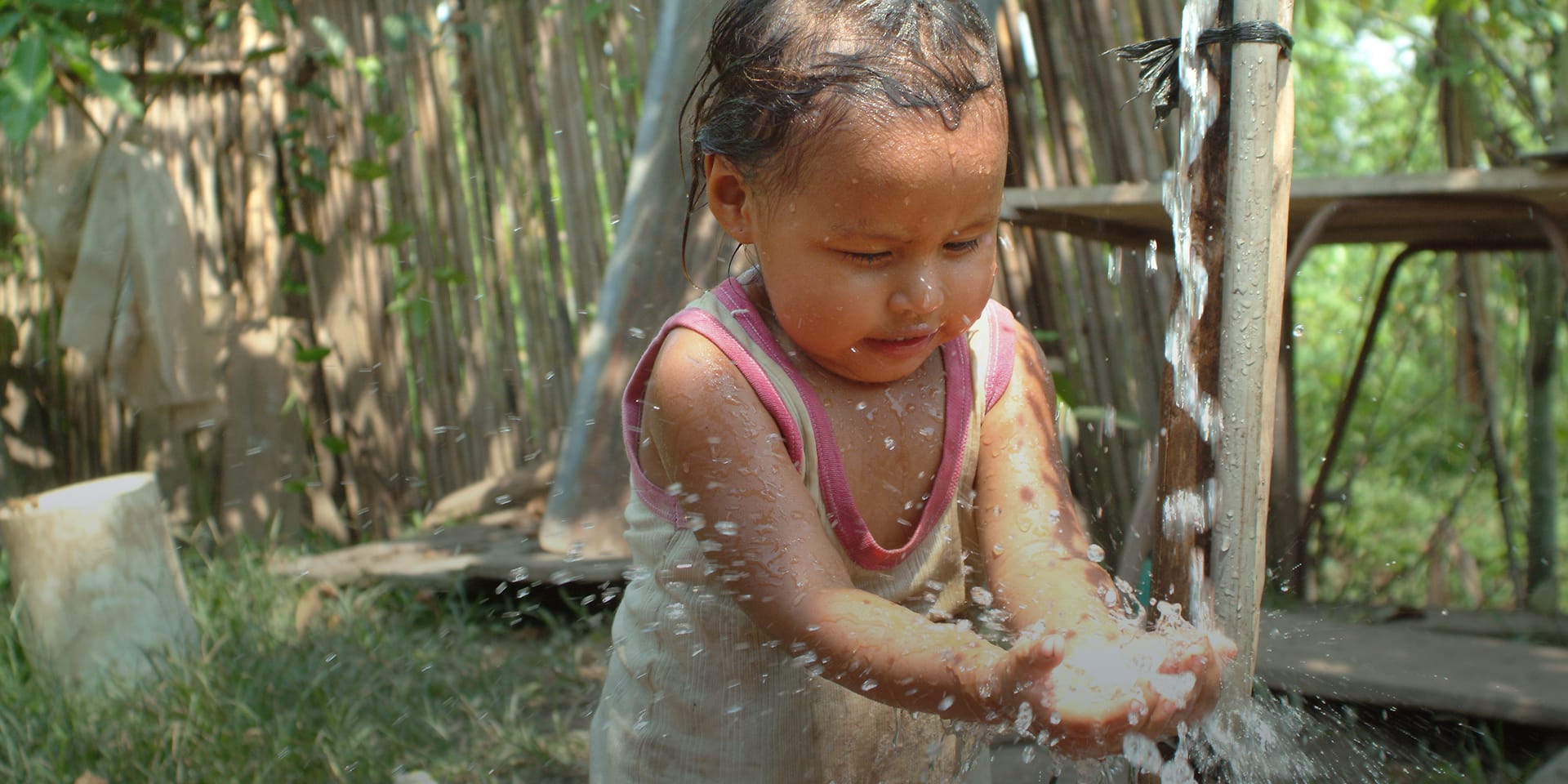 A toddler holding her hands out as water from a spout splashes over them.