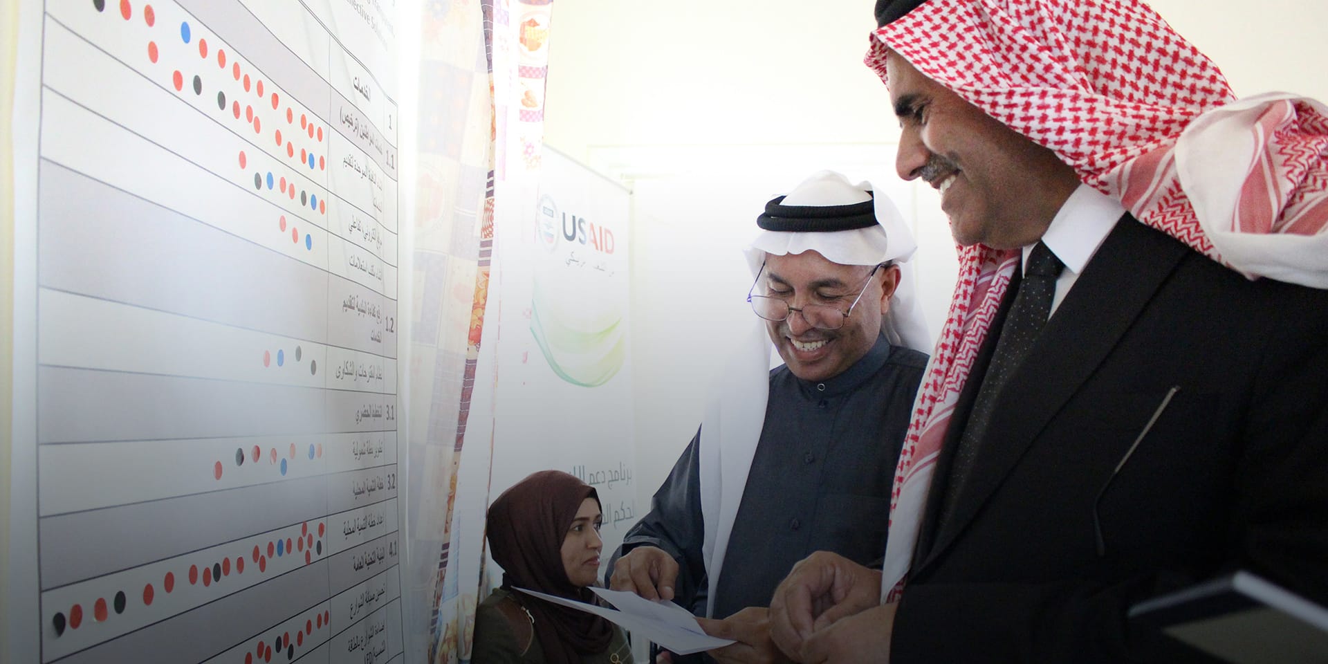 Two people smiling as they discuss a chart on the wall in front of them.