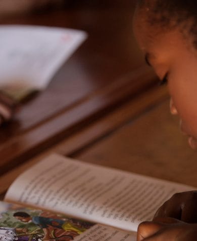 A young girl sitting at a school desk and reading a book.
