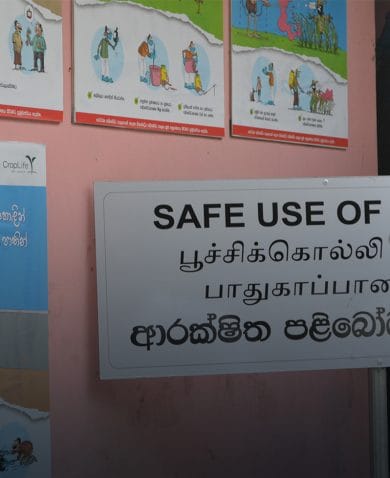 A man looking at a poster showing a cartoon of a person reaching for pesticide next to a sack of grain. A sign the man reads "Safe Use of Pesticides."