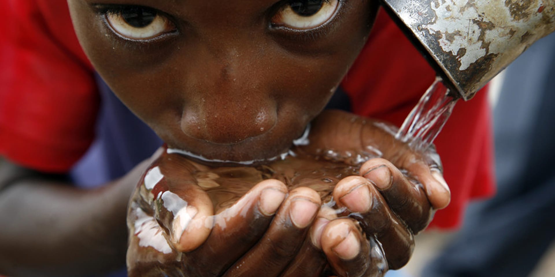 Close-up image of a young boy drinking water pouring into his hands from a waterspout.