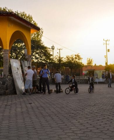 Image of a paved city center with several people painting large portraits that are leaning against a gazebo.
