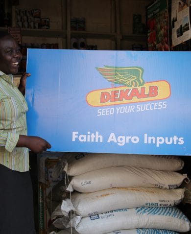 A smiling woman holding up a large sign that says "Dekalb: Seed your Success; Faith Agro Inputs."