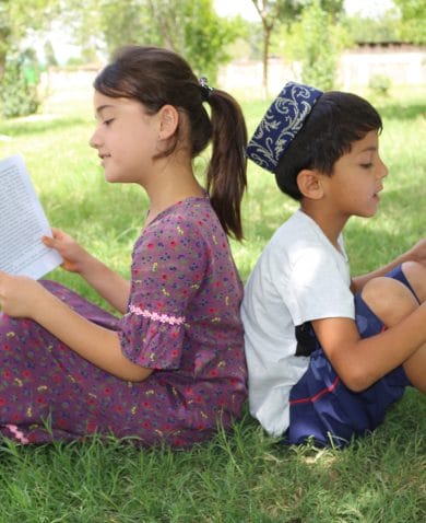 Image of a boy and a girl sitting in grass with their backs to each other. Each is reading a book.