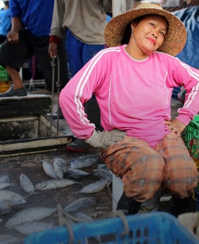 A woman posing for a photo as she sits in a market selling fish.