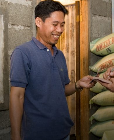 Two men smiling and exchanging information as they stand next to sacks filled with hog feed.