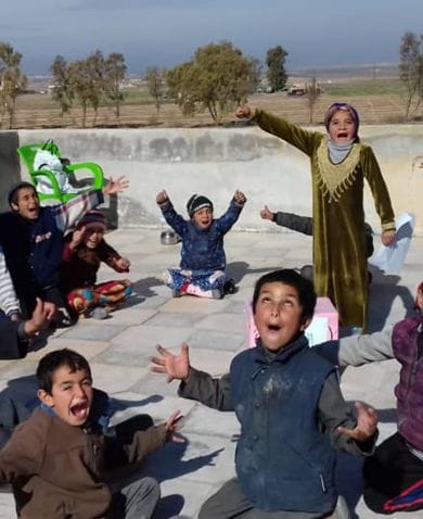 Syrian children sitting in a circle shout happily