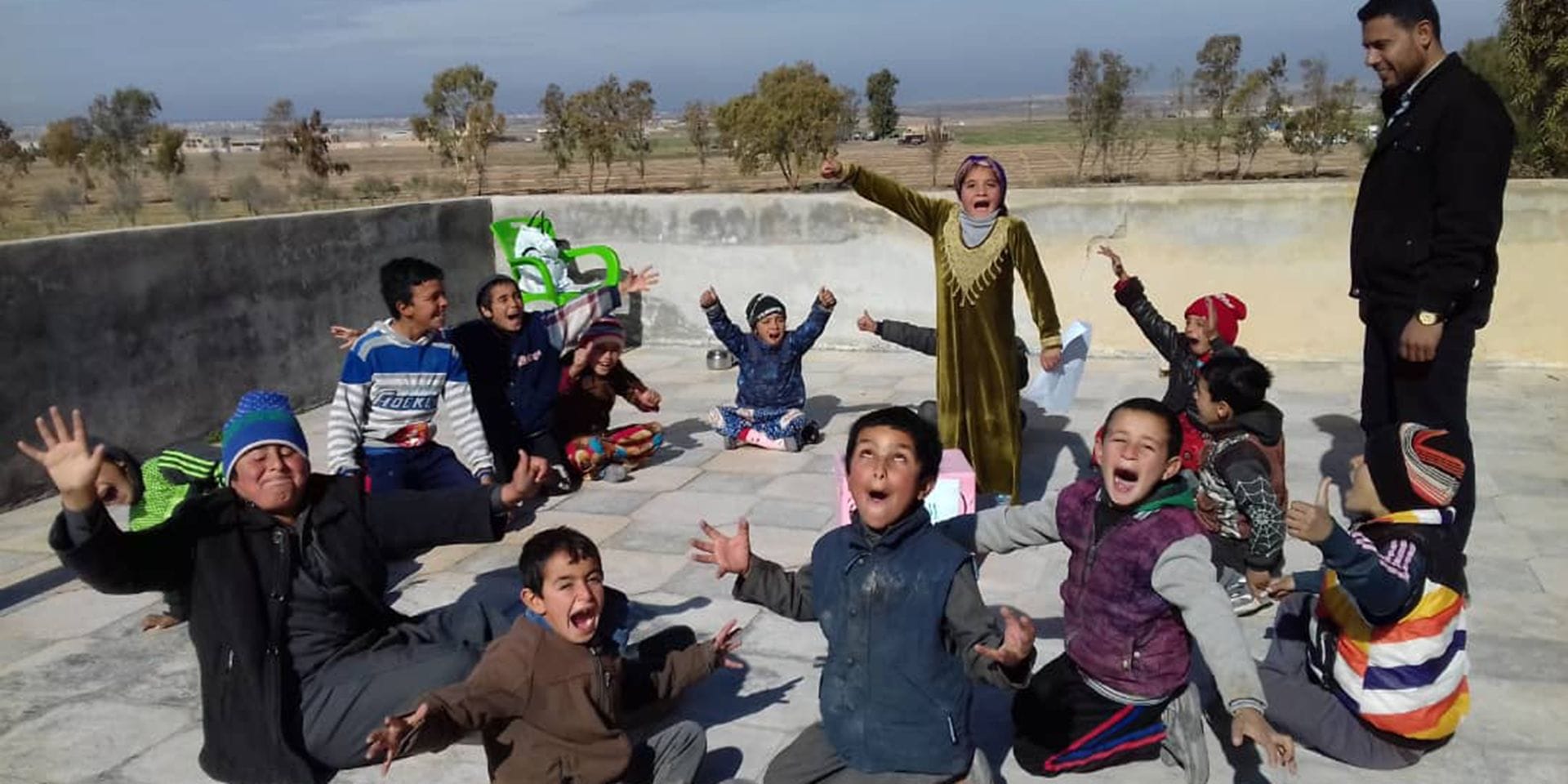 Syrian children sitting in a circle shout happily