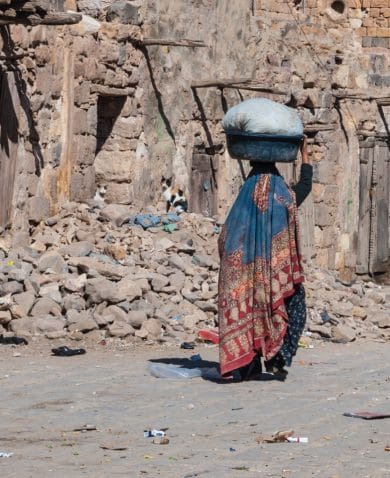 A woman with a basket on her head walks down a road in Sanaa, Yemen.