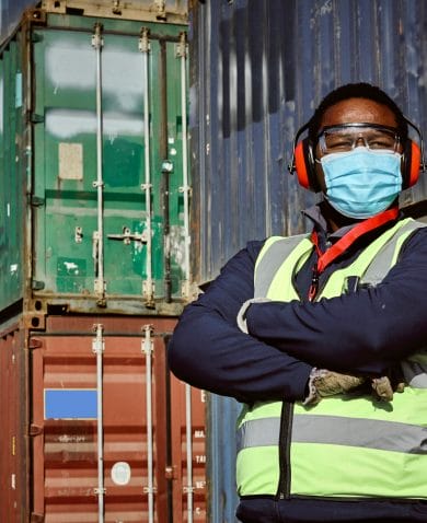 A man assessing and accounting for shipping containers in a storage yard in Johannesburg South Africa. He is wearing a reflective vest and a face mask.