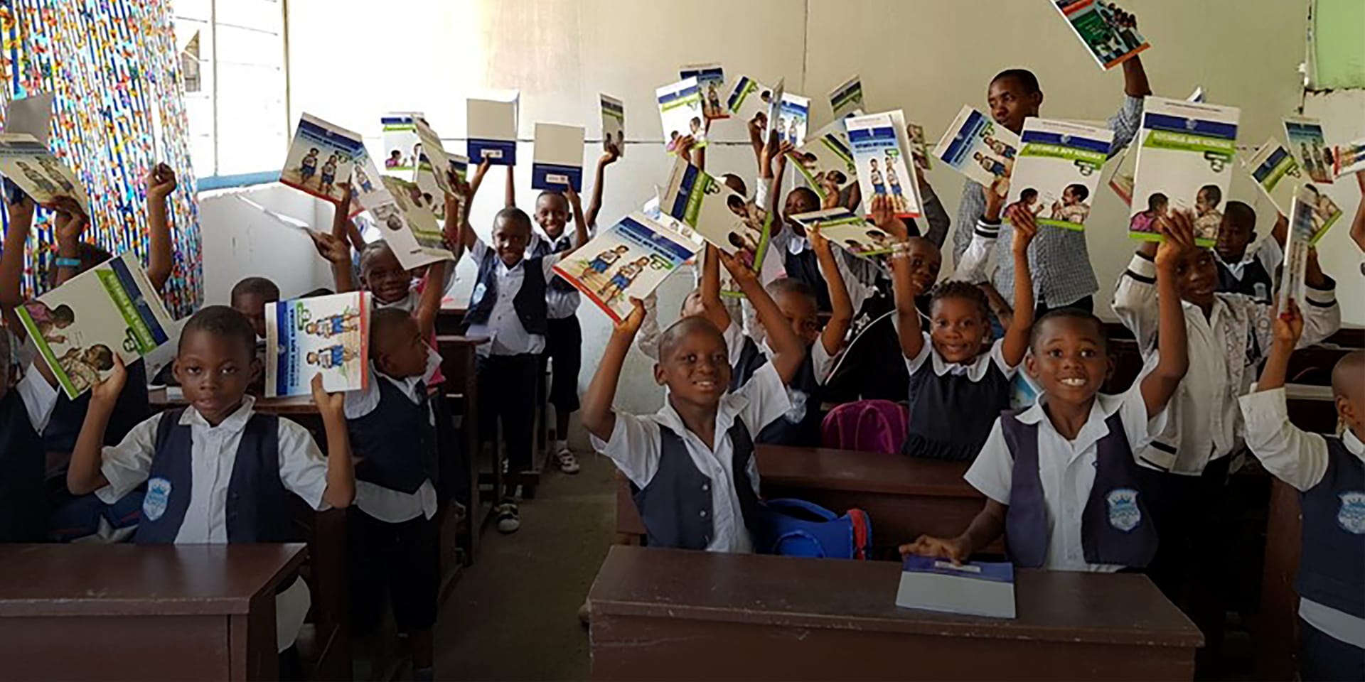 Children lift textbooks happily above their heads.