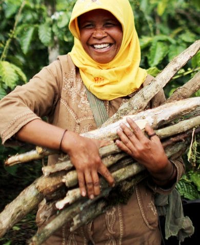 A woman smiling as she carries a bundle of sticks.