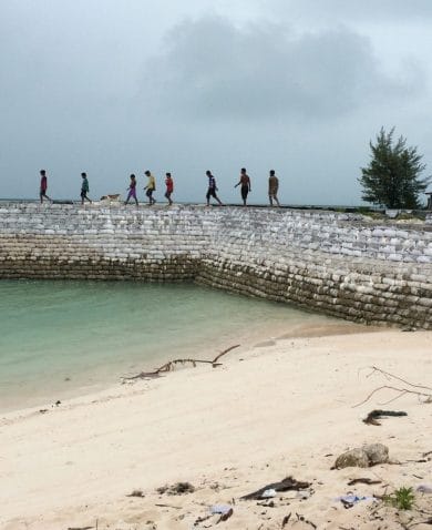 A group of young people walk along a sea wall in Tarawa, Kiribati.