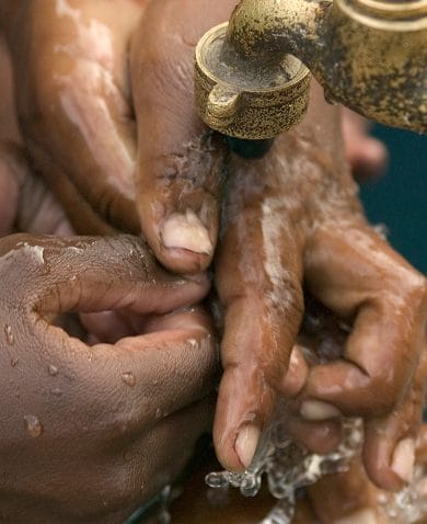 An image of several pairs of hands washing under a waterspout.