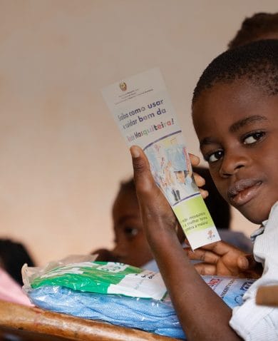 Student in Mozambique holds bed net and pamphlet about malaria.