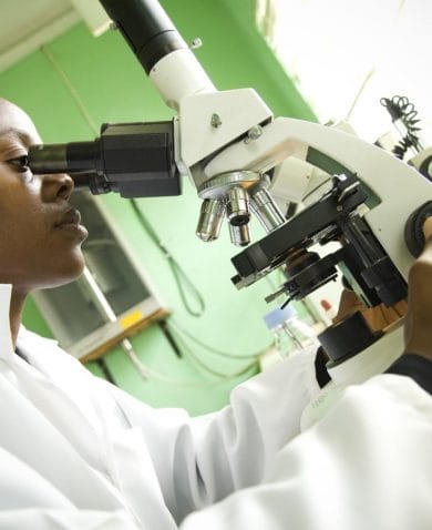 Researcher in a white lab coat looks through a microscope.