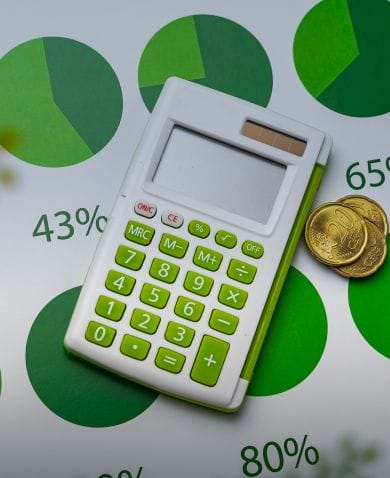 A calculator sits on a table on top of green-colored pie-charts and coins.
