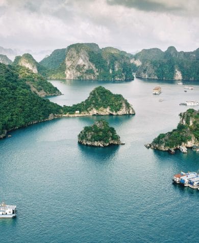 An aerial view of Halong Bay in Vietnam. Several boats can be seen traveling between green, mountainous islands.